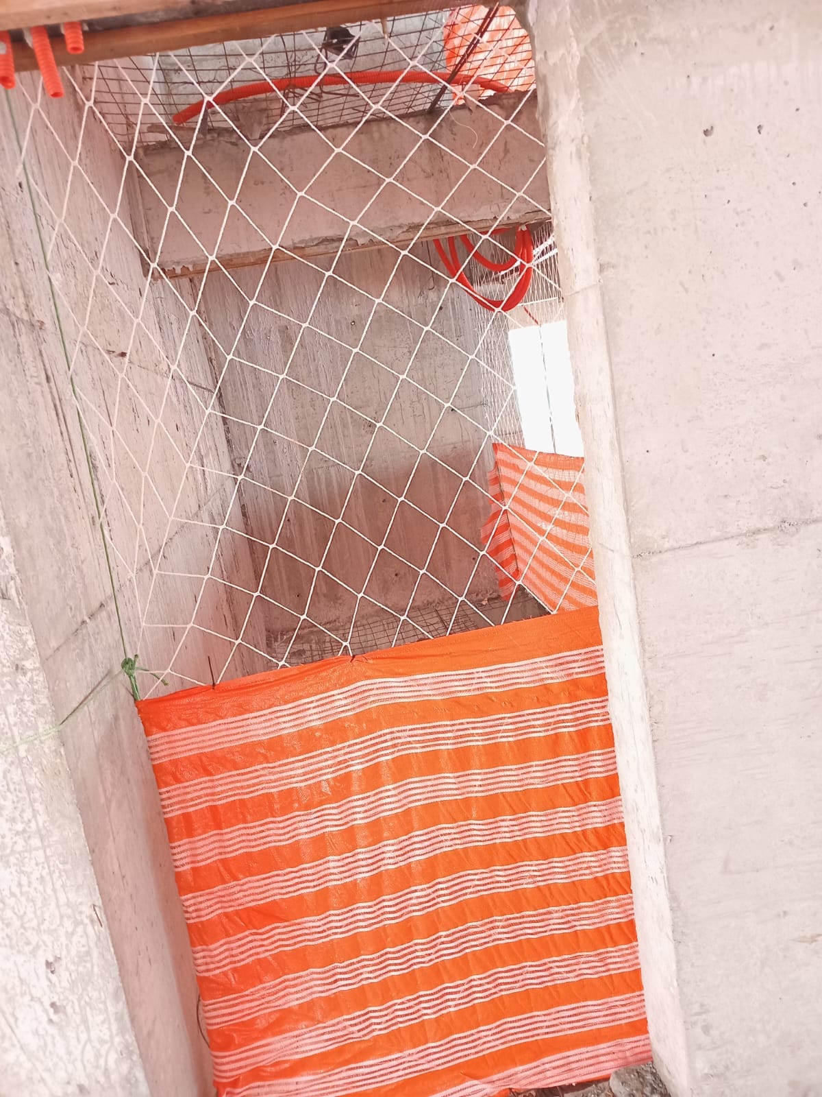 Rede de proteção instalada em vão entre lajes de obra em construção, com tela alaranjada de contenção abaixo