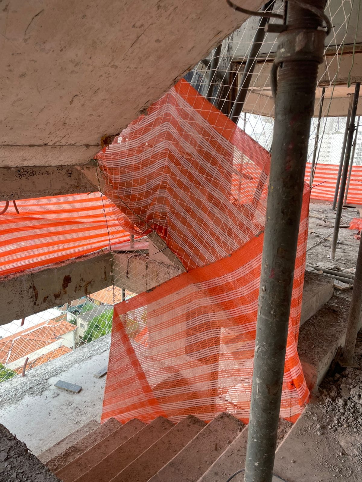 Rede de proteção fixada em abertura entre pavimentos, com vista para telhados e prédios do entorno