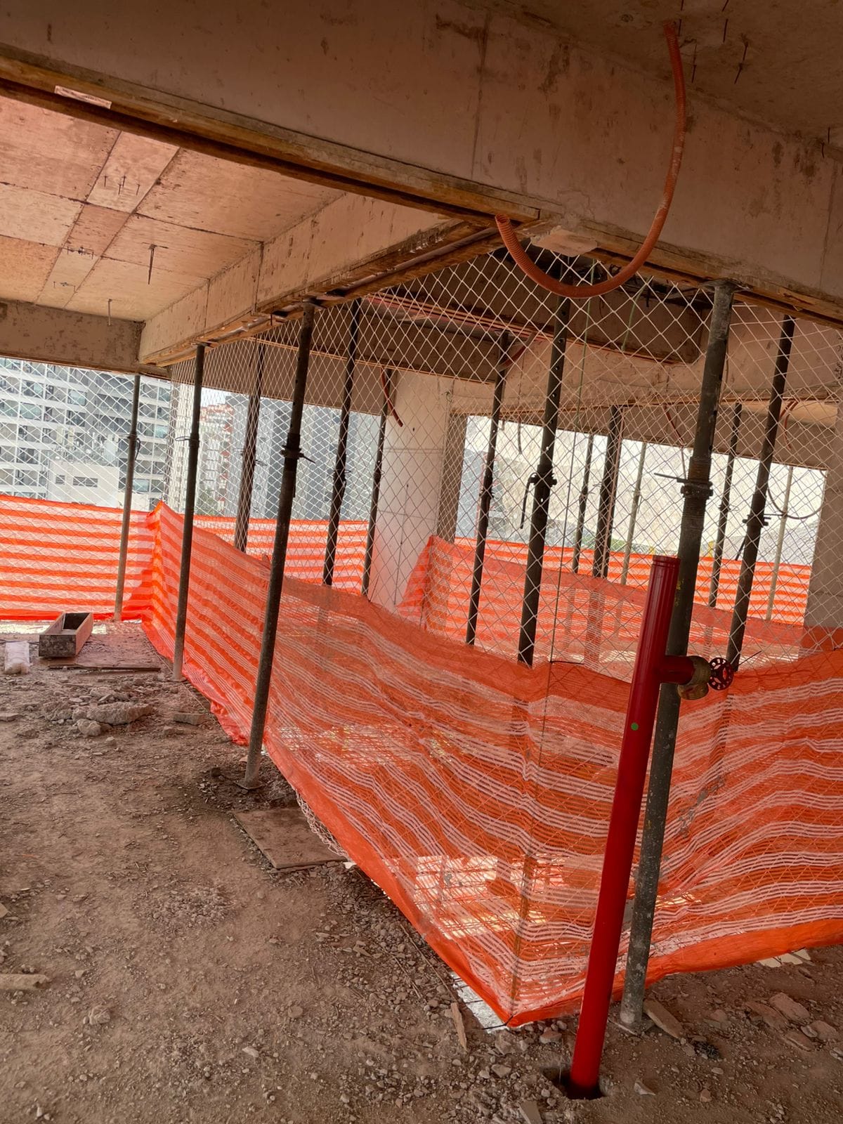 Rede de proteção instalada ao longo de pavimento aberto em obra, com tela de contenção e estrutura metálica de apoio