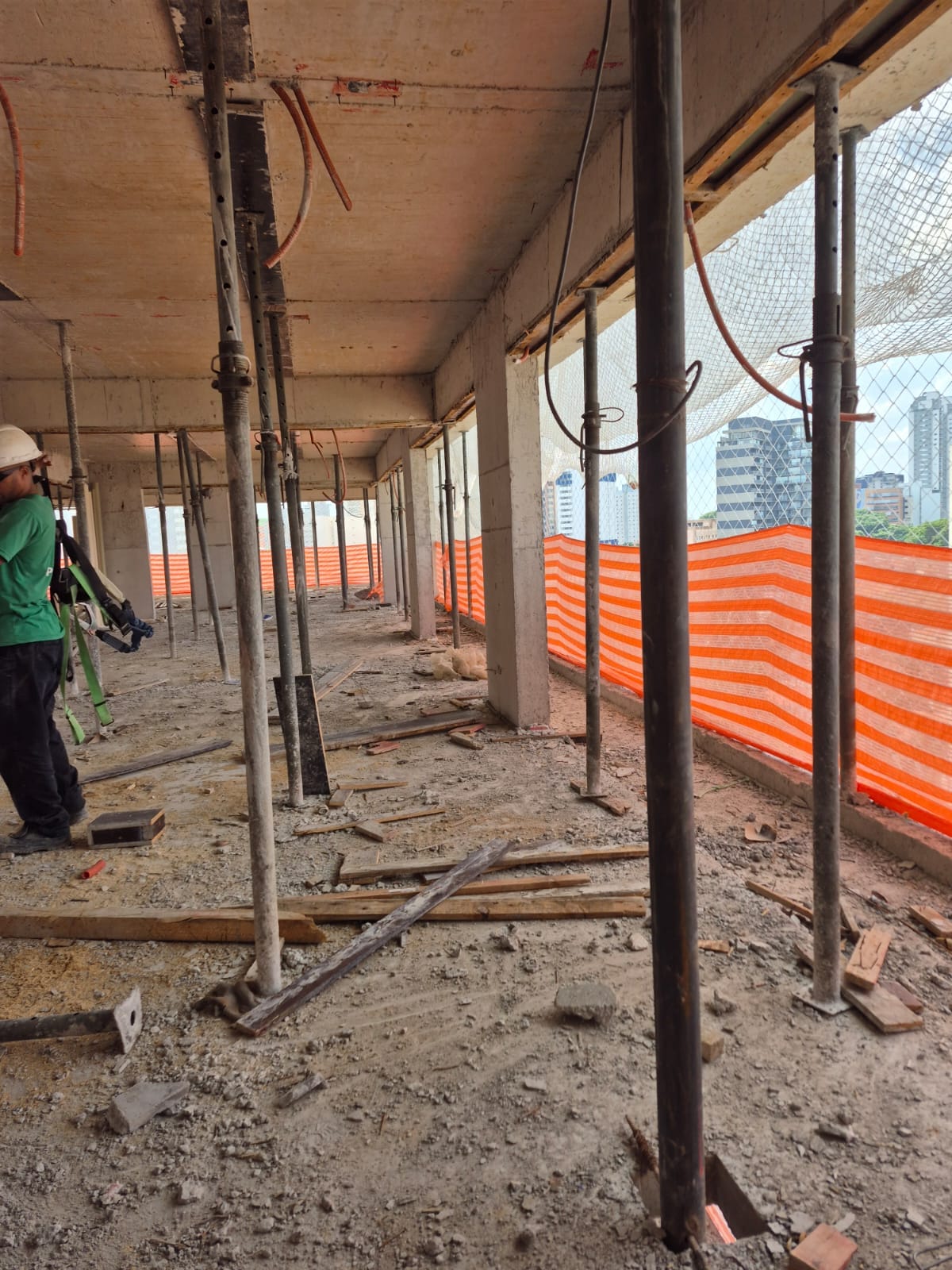 Rede de proteção em pavimento de obra com trabalhador de capacete e cinto de segurança ao lado da tela de contenção