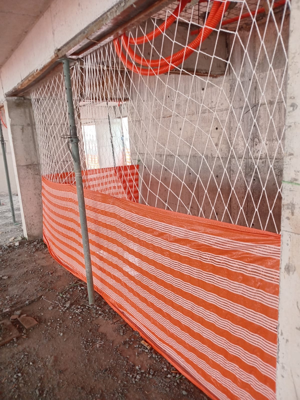 Rede de proteção e tela alaranjada instaladas em abertura de pavimento, com janela ao fundo