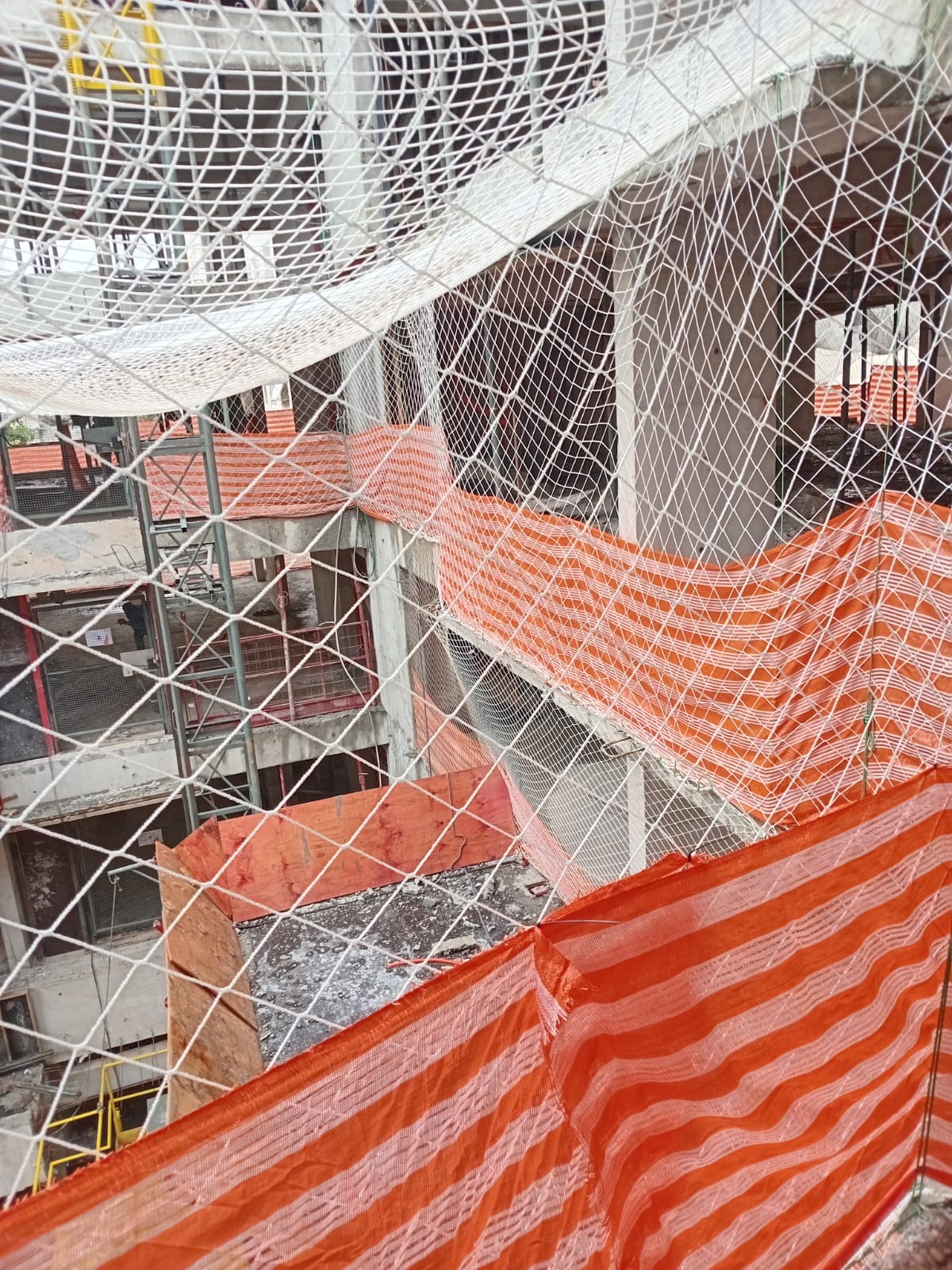Vista de cima da rede de proteção cobrindo várias aberturas de pavimentos em obra, com tela alaranjada e andaimes