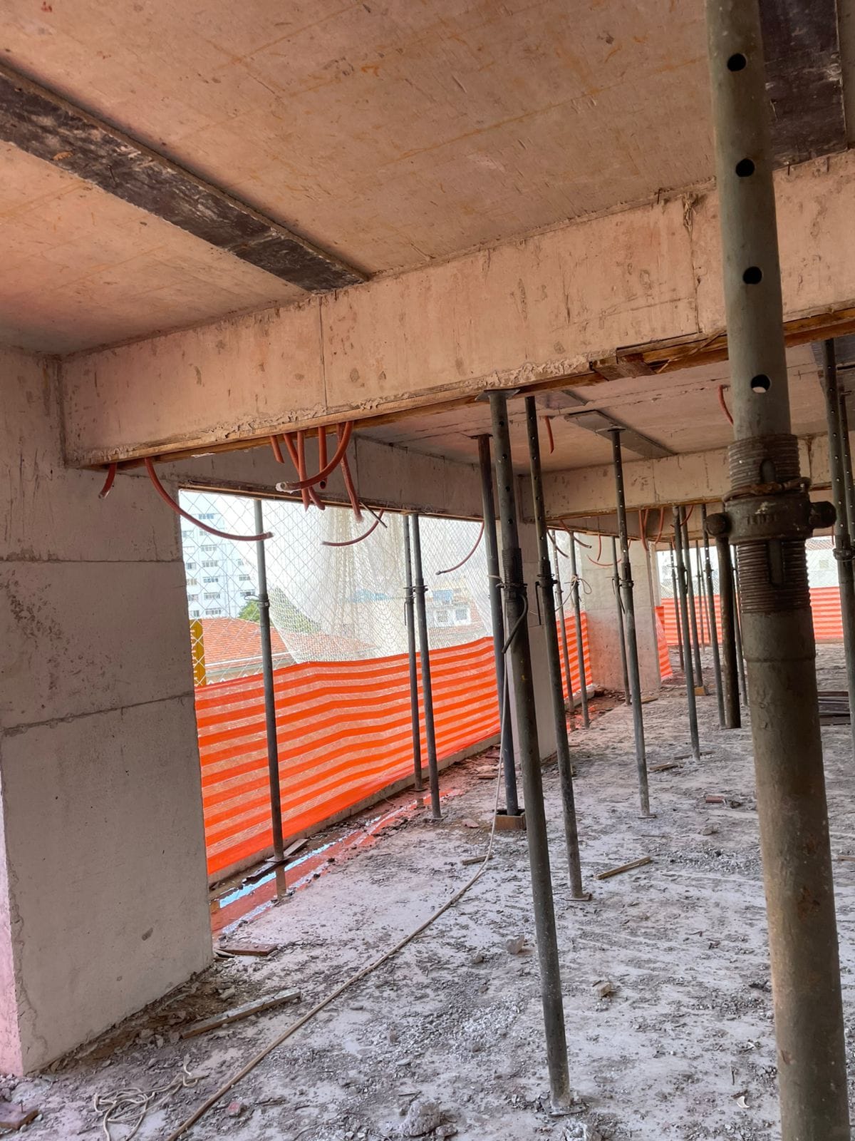 Rede de proteção instalada em abertura de pavimento com tela alaranjada e tubulações elétricas aparentes