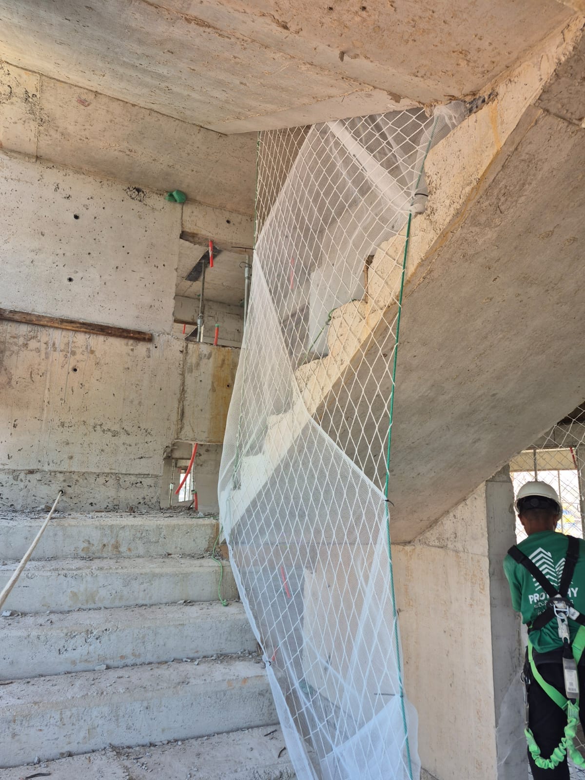 Rede de proteção instalada em vão de escada em obra, com trabalhador de capacete e cinto de segurança