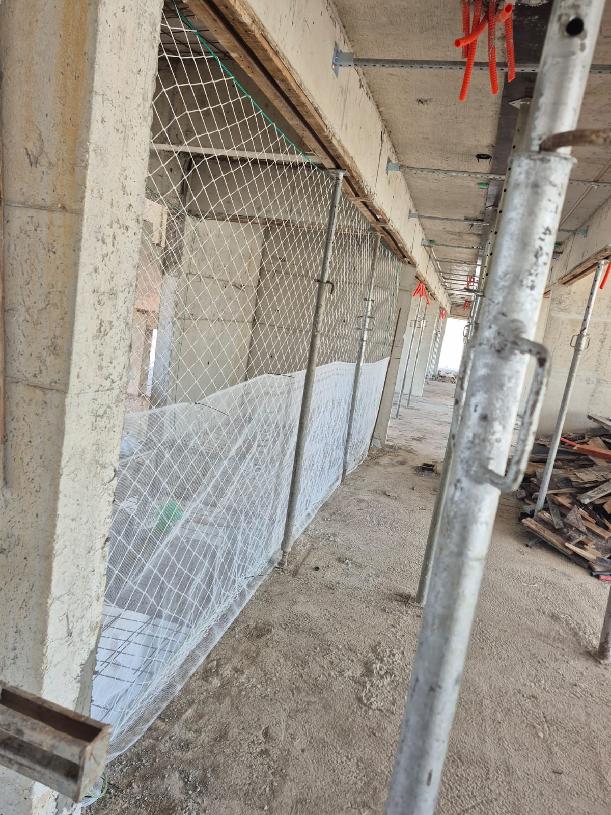 Rede de proteção instalada em abertura de corredor de obra, com pallets de madeira ao lado