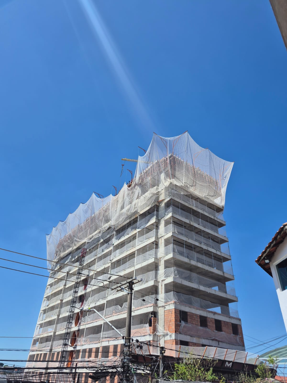 Fachada de prédio em construção com rede de proteção SLQA no topo e alvenaria aparente nos andares inferiores