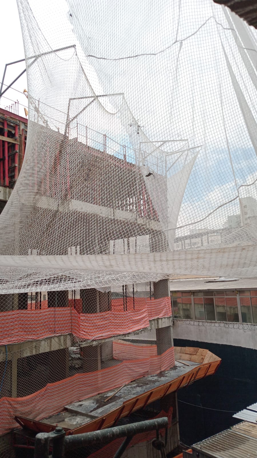 Estrutura de sustentação da rede de proteção SLQA vista de dentro da obra, com telas alaranjadas nos pavimentos