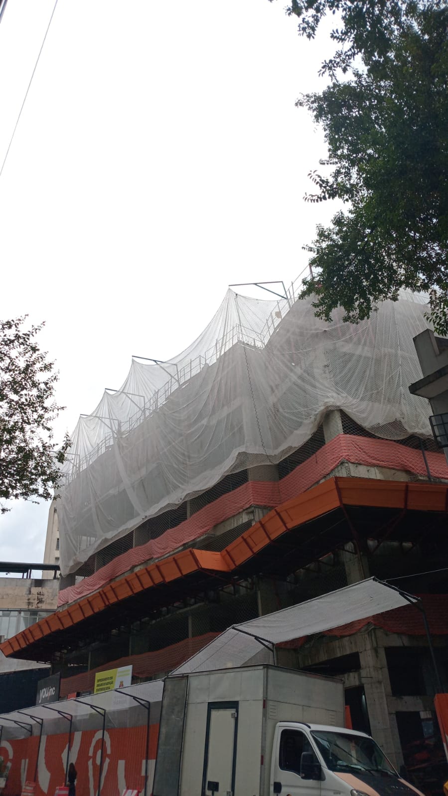 Vista da rua de prédio em construção com sistema SLQA de rede de proteção cobrindo a fachada
