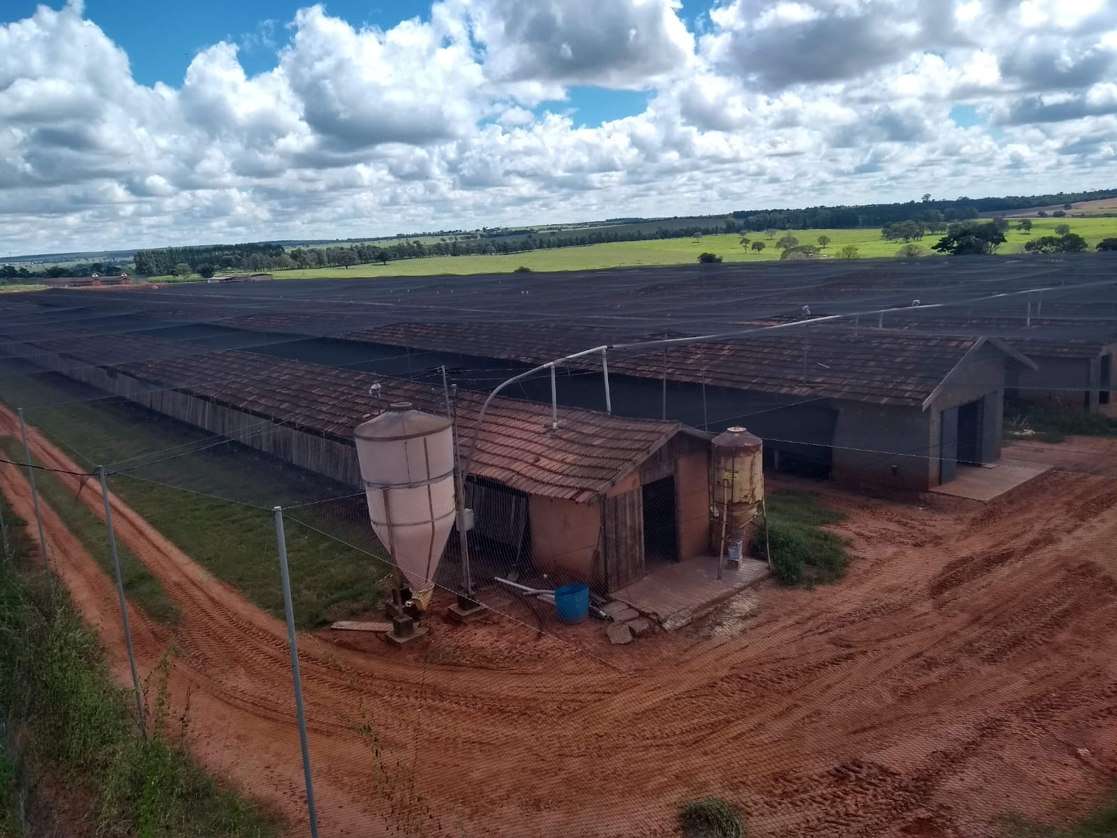 Vista aérea de galpões agrícolas cobertos por tela de sombreamento em área rural